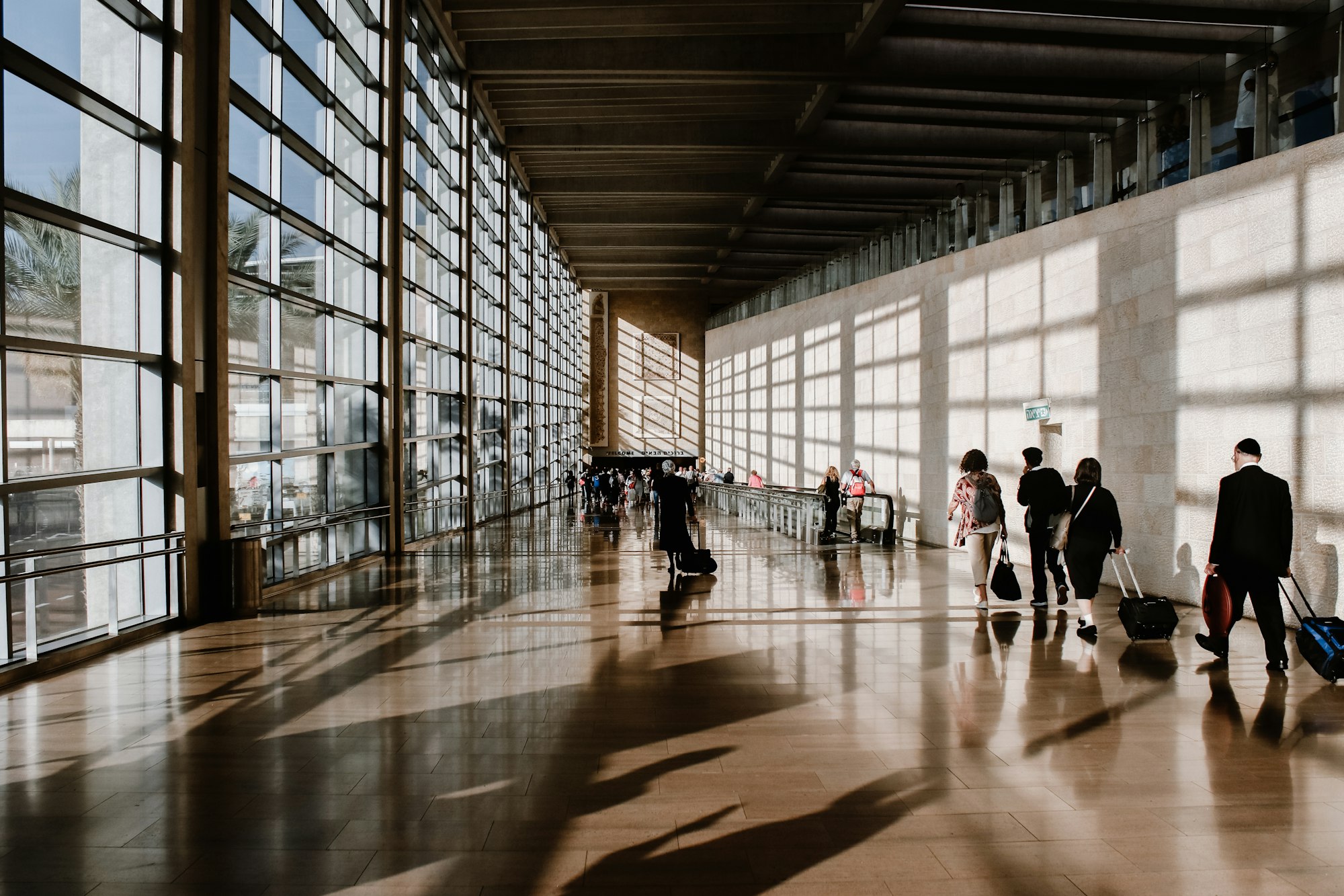 Travellers with luggage walking through a sunlit airport terminal