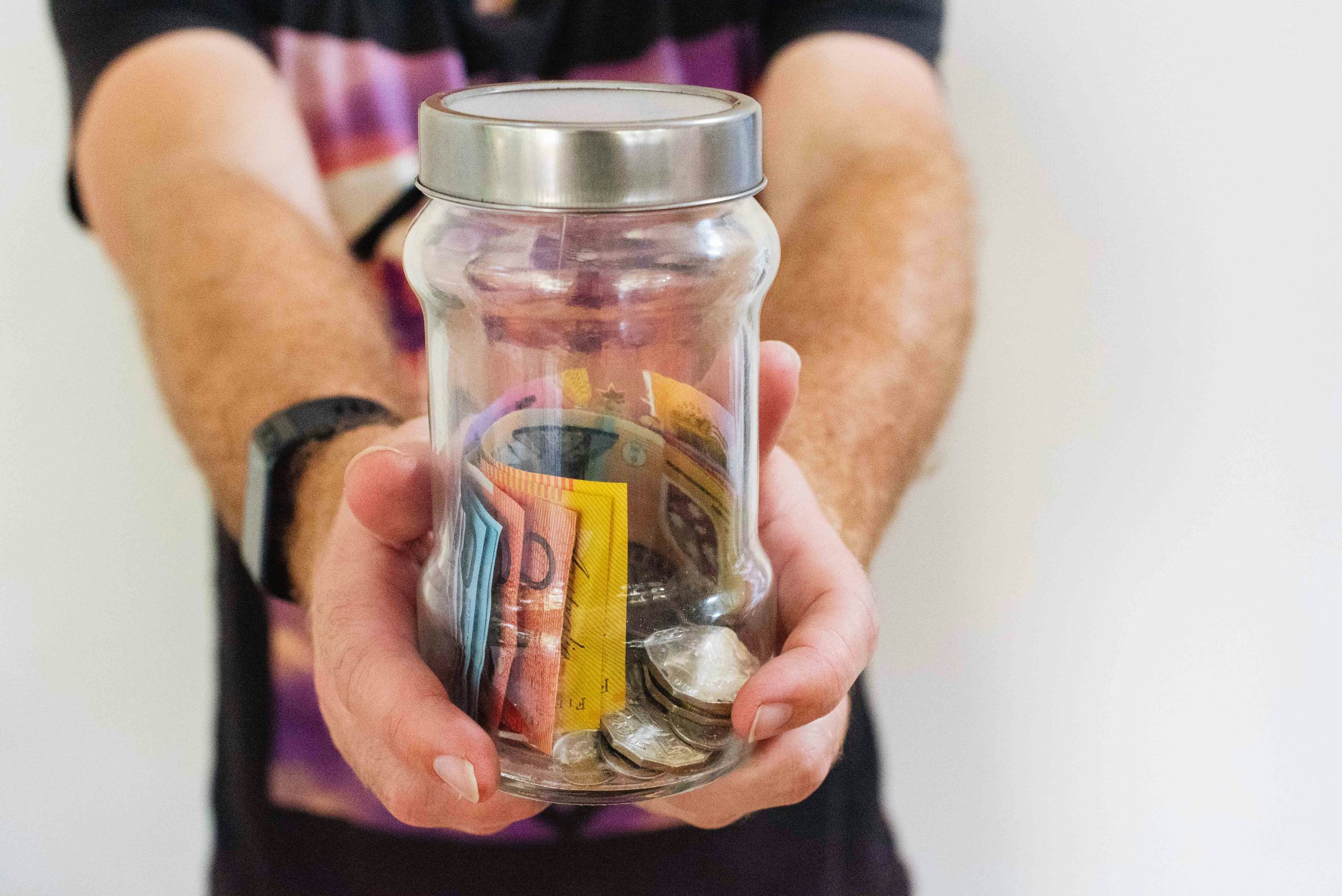 Hands holding a glass jar of coins and banknotes