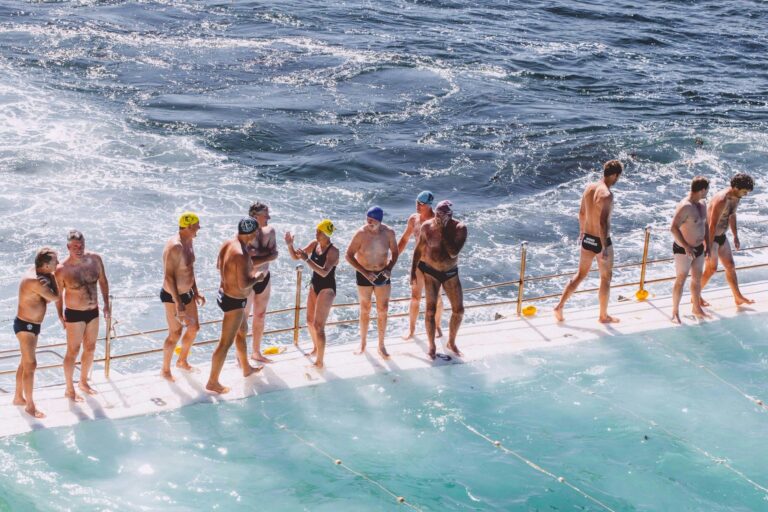 Swimmers lined up on the edge of an ocean pool as waves break