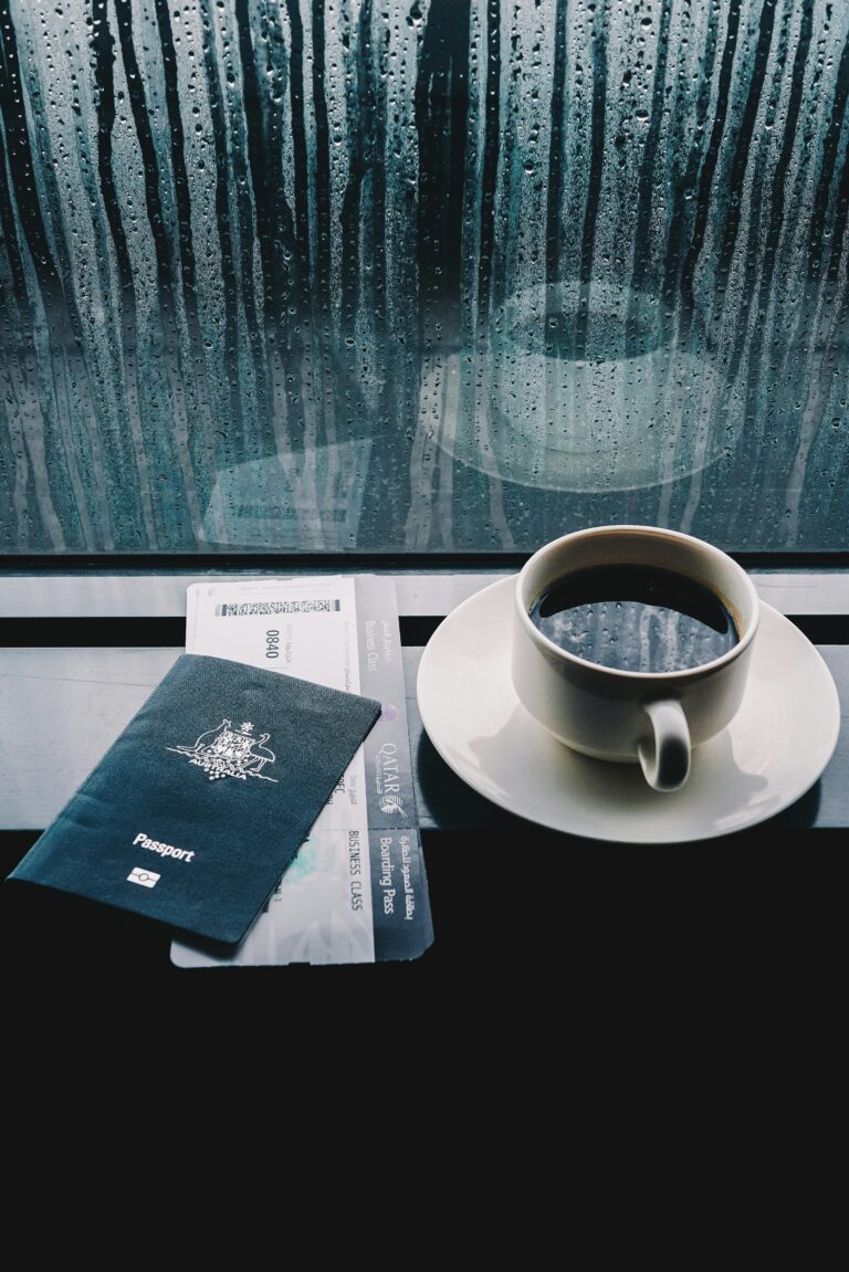 A passport beside a cup of coffee at a rain-streaked airport window